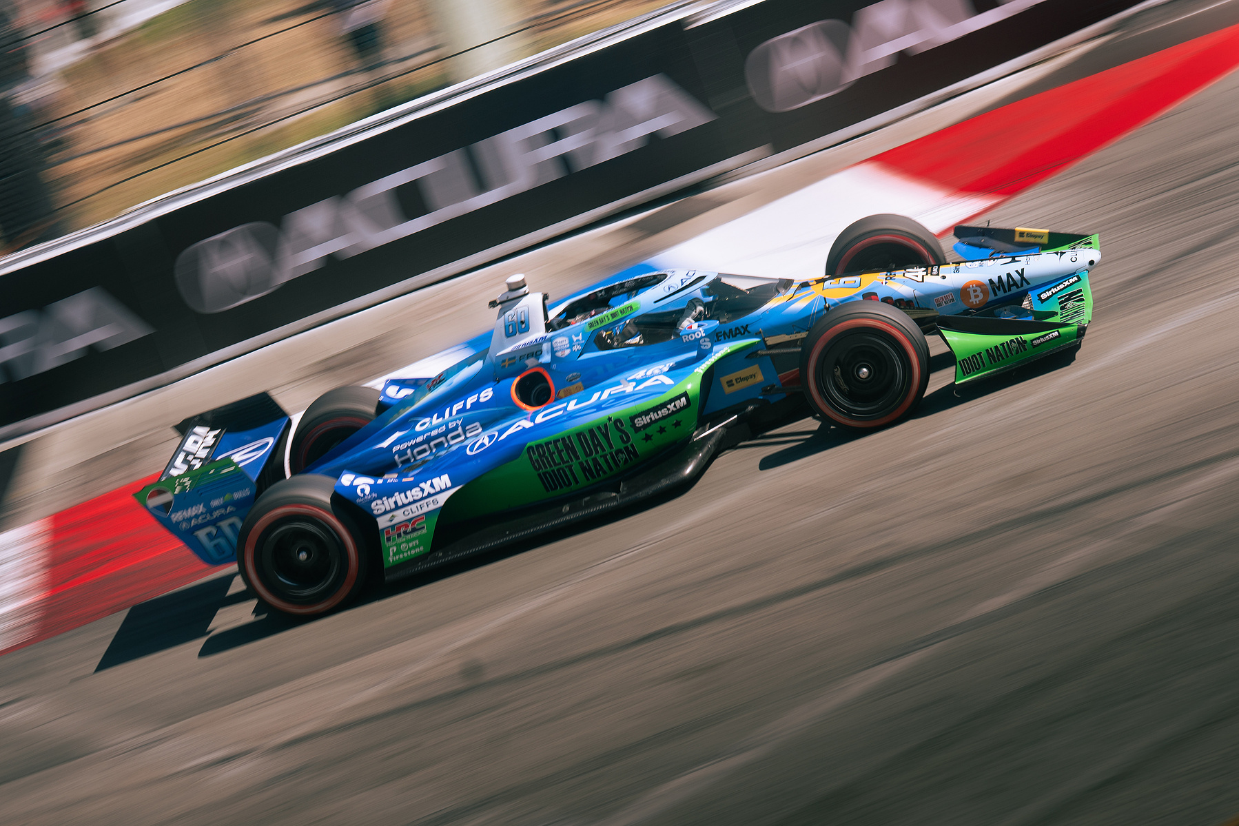 An IndyCar passes the Long Beach barriers in a diagonal panning photograph.