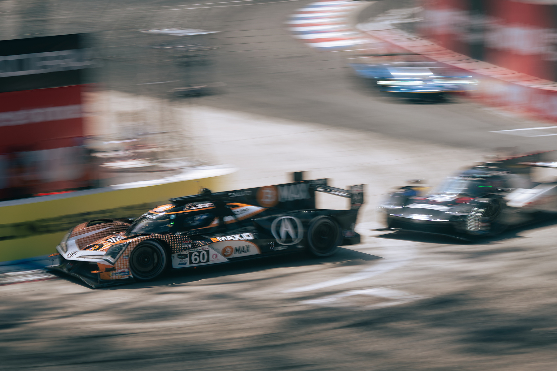 Acura prototypes race through a street-circuit corner in a panning photograph.