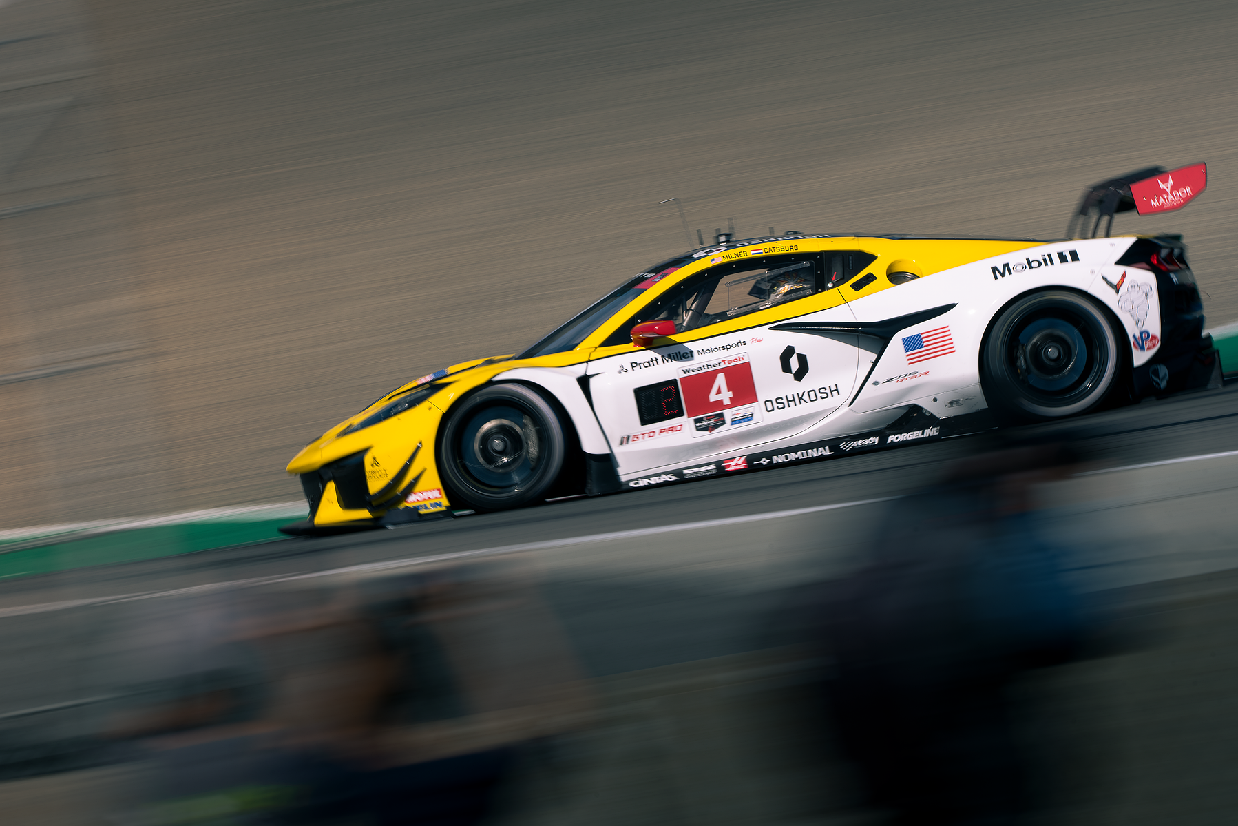 A yellow and white Corvette race car passes in a panning photograph at Laguna Seca.