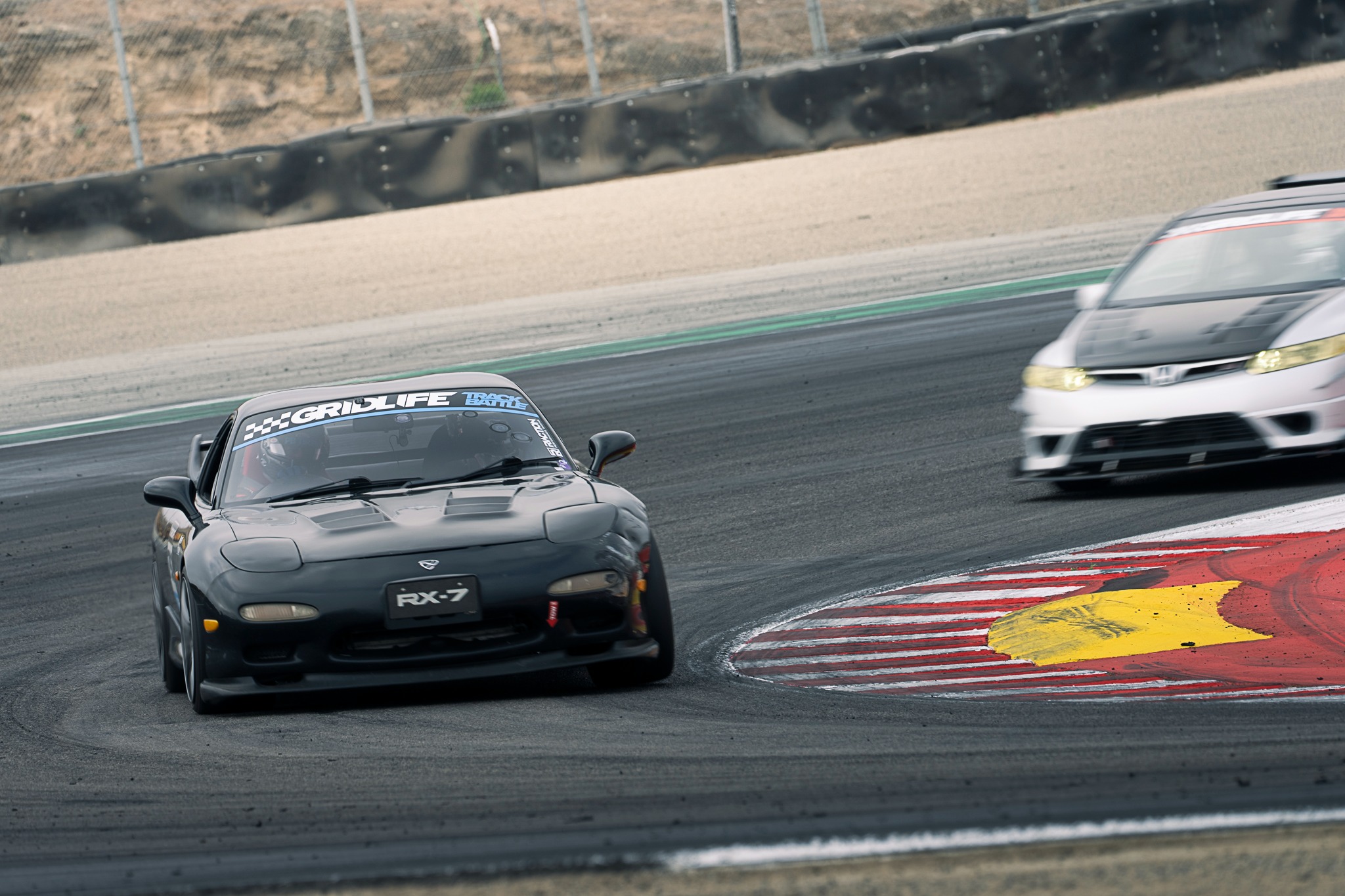 A dark sports car leads another car through a corner at Laguna Seca.