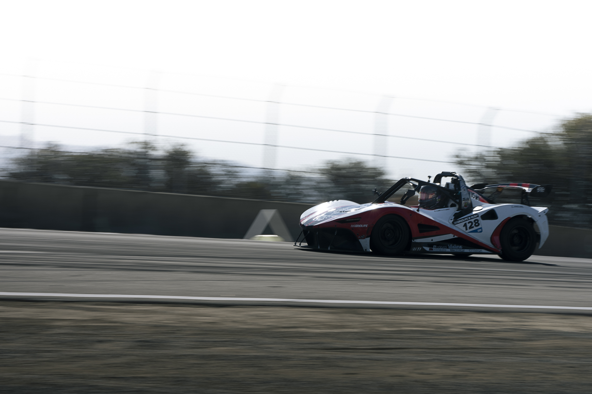 An open-cockpit race car passes at speed at Laguna Seca.