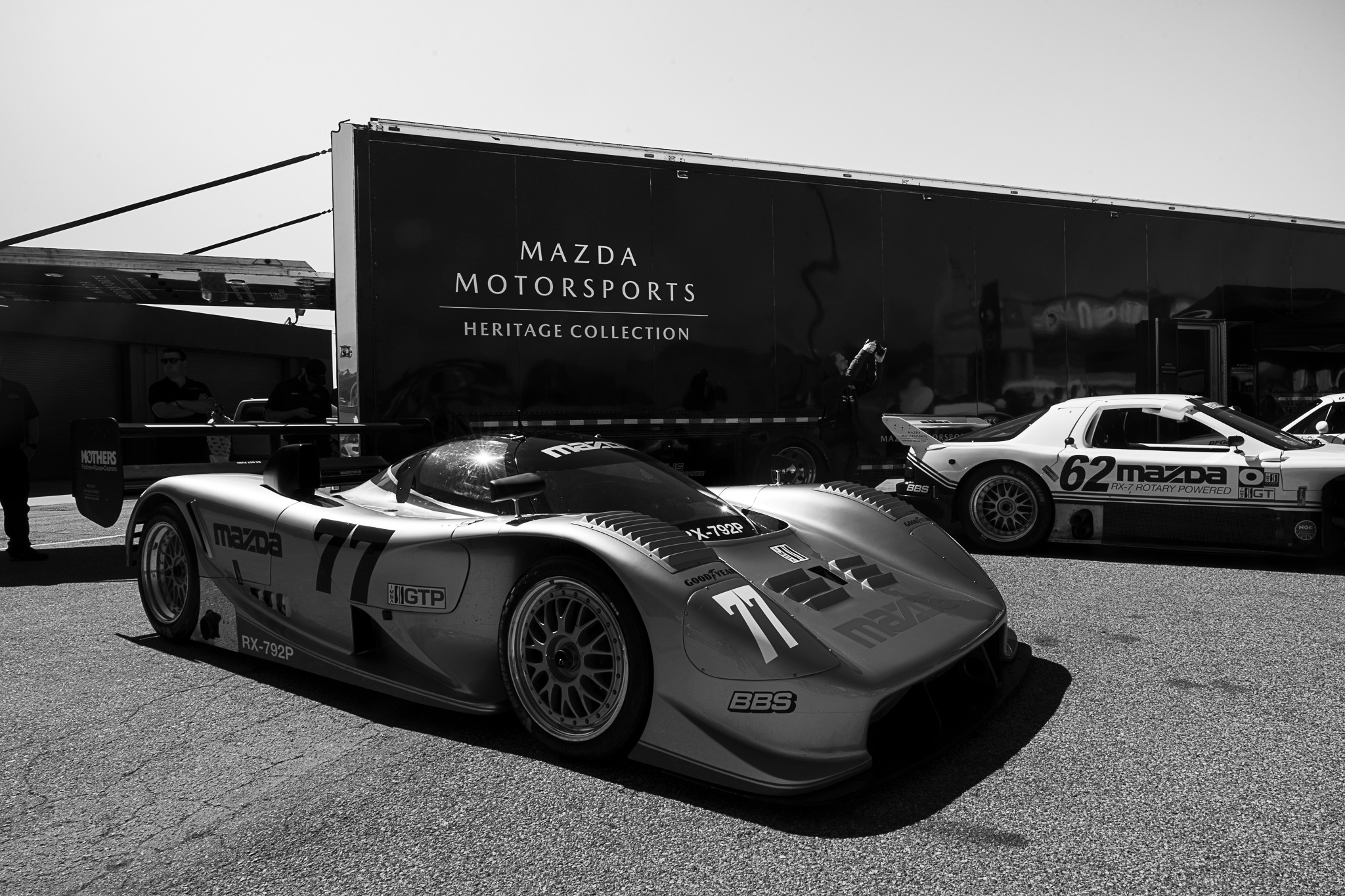 Black-and-white photograph of race cars in the Laguna Seca paddock.