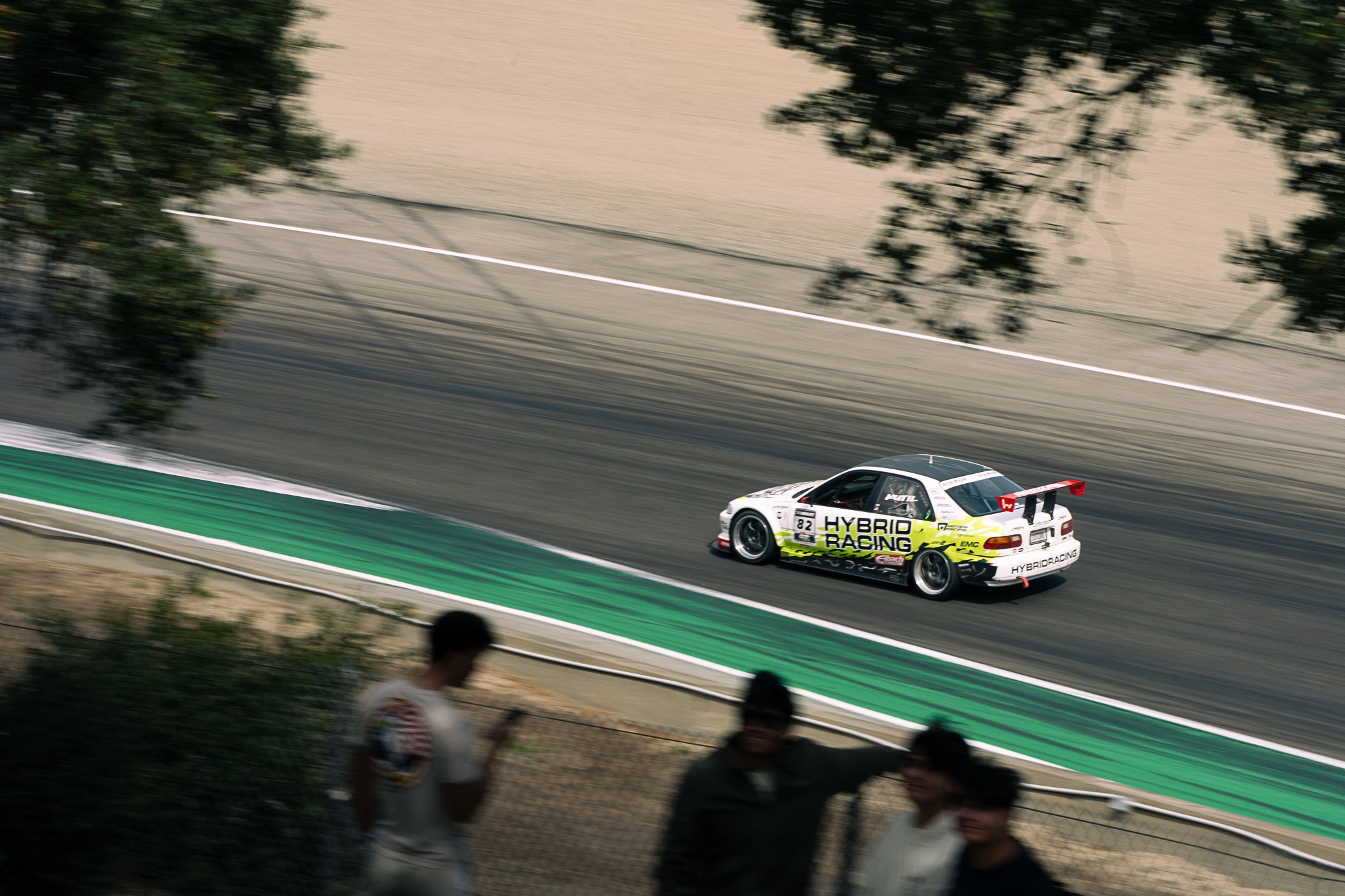 Spectators watch a race car on track through the trees at Laguna Seca.