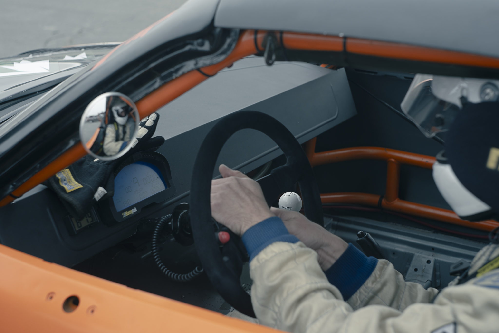 A view into a race car cockpit with a driver at the steering wheel.