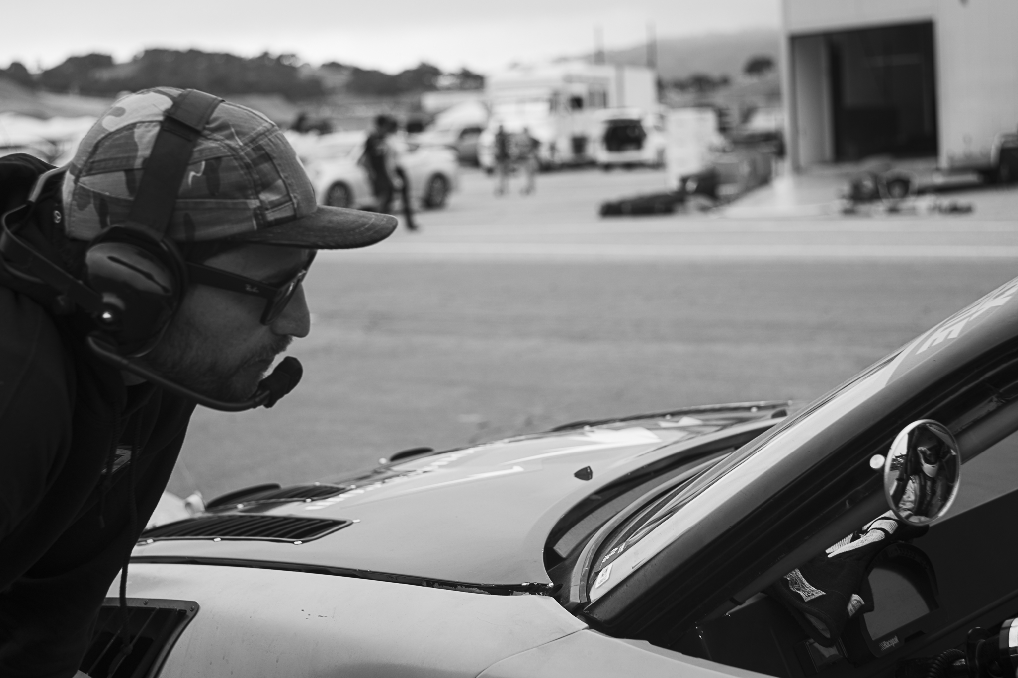 Black-and-white paddock portrait of a person wearing a headset beside a race car.
